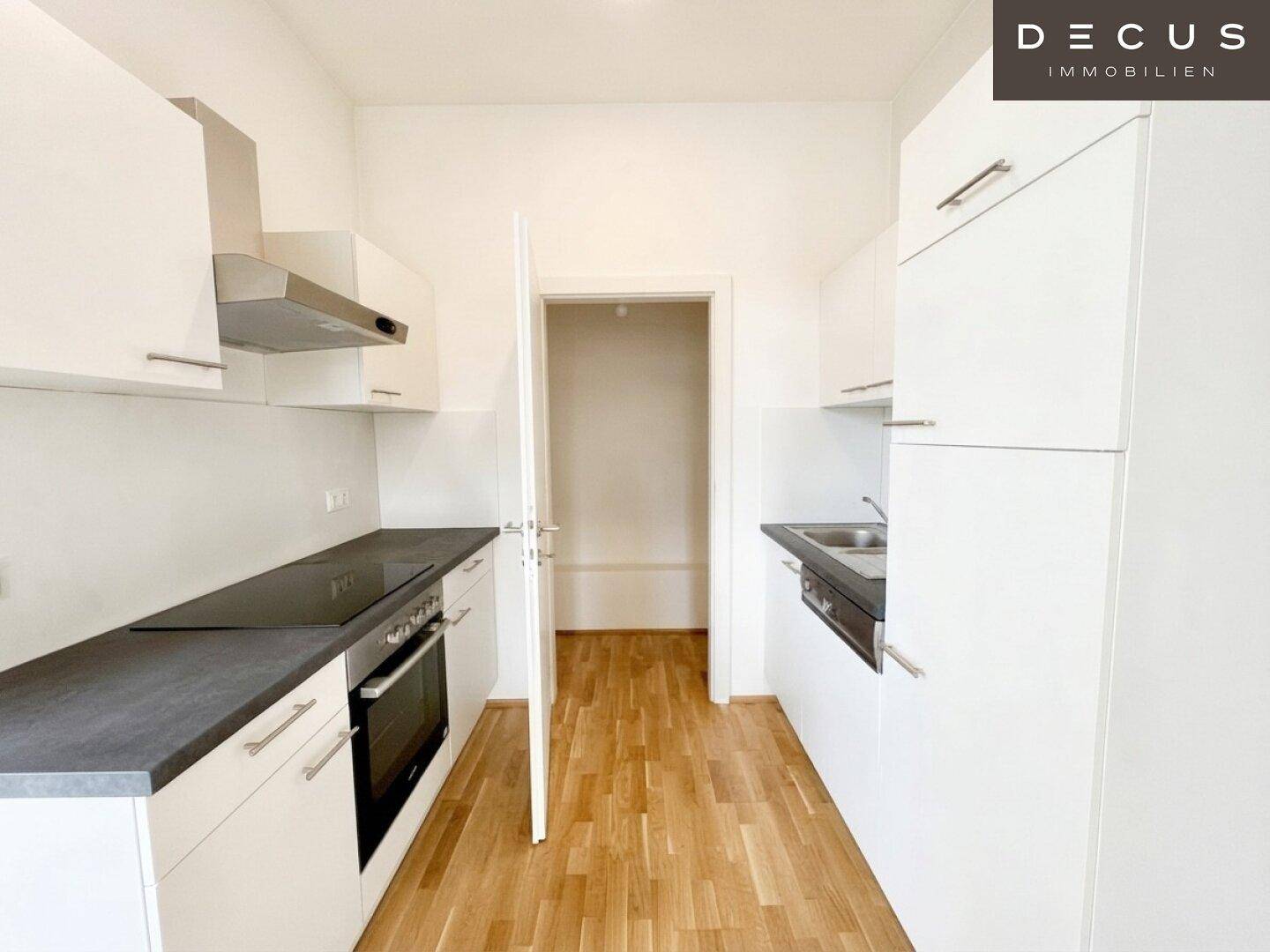 Schmale, moderne Küche mit weißen Schränken, dunkler Arbeitsplatte und Holzboden.