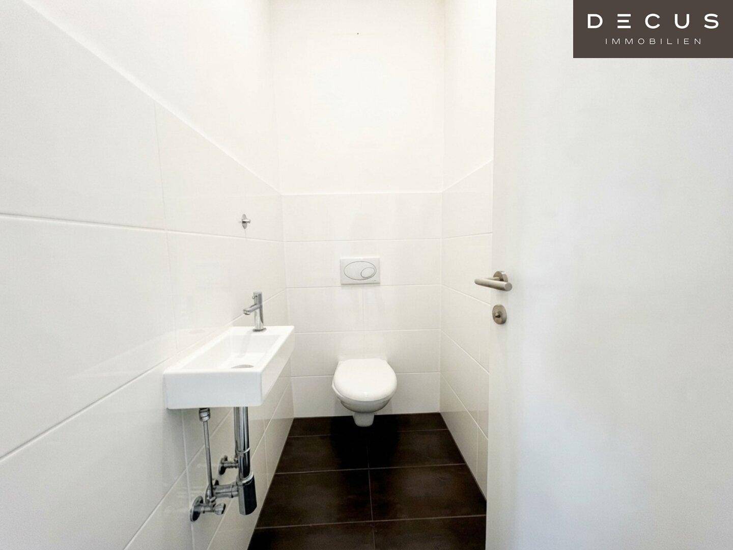 Separates Gäste-WC mit wandhängender Toilette, kleinem Waschbecken und dunklem Fliesenboden.
