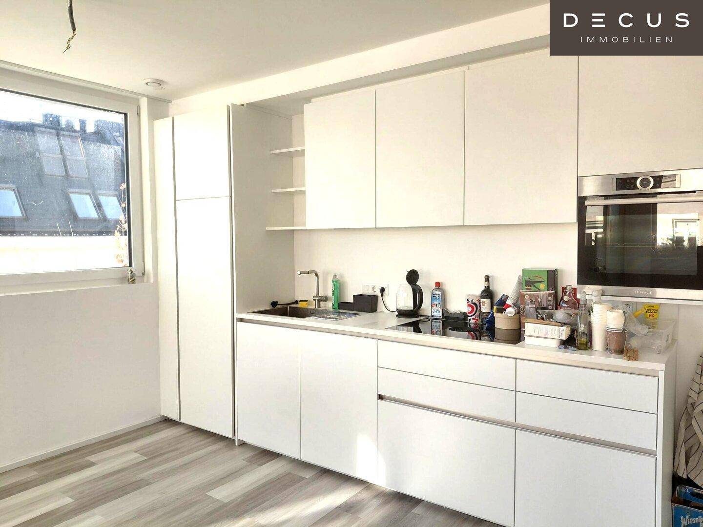 Moderne weiße Küche mit Einbaugeräten, viel Stauraum und Fenster für Tageslicht.