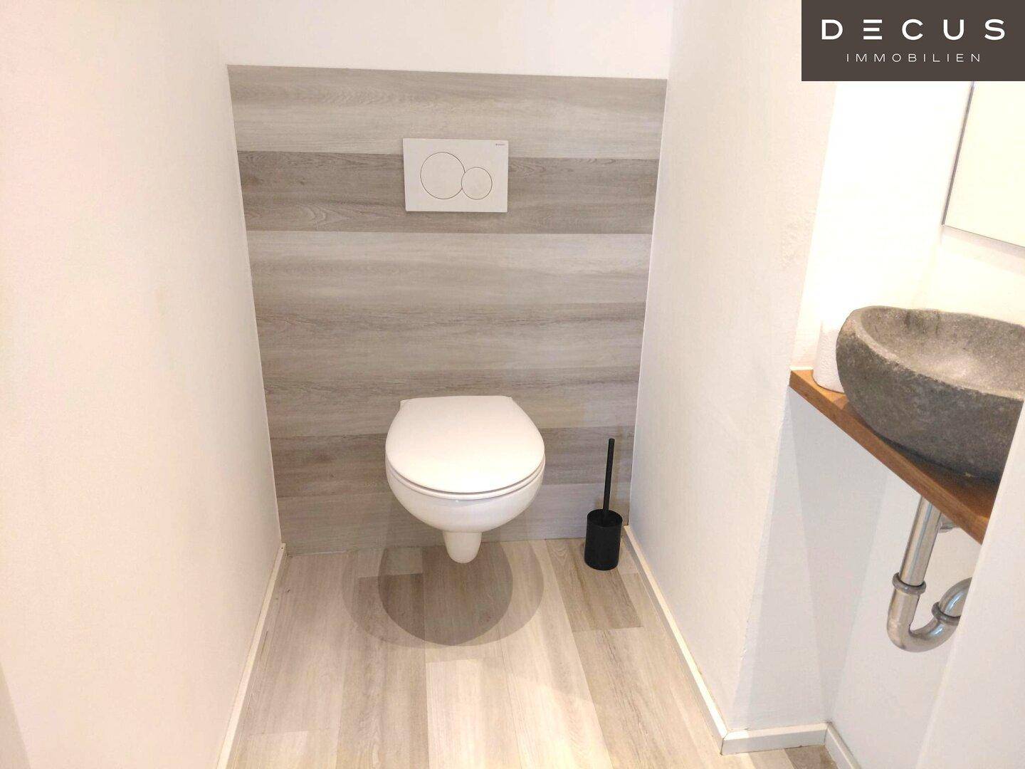 Kompaktes Gäste-WC mit Wand-WC und einem stilvollen Natursteinwaschbecken auf Holzkonsole.