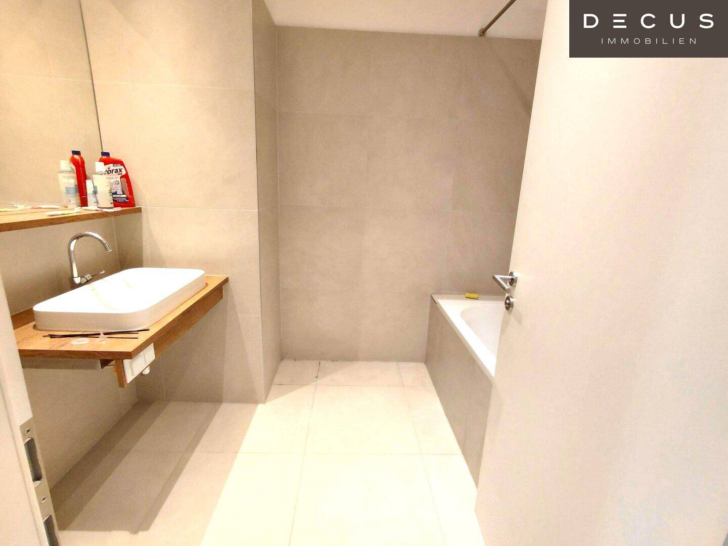 Modernes Badezimmer mit hellen Fliesen, einer Badewanne und einem schwebenden Waschbecken.