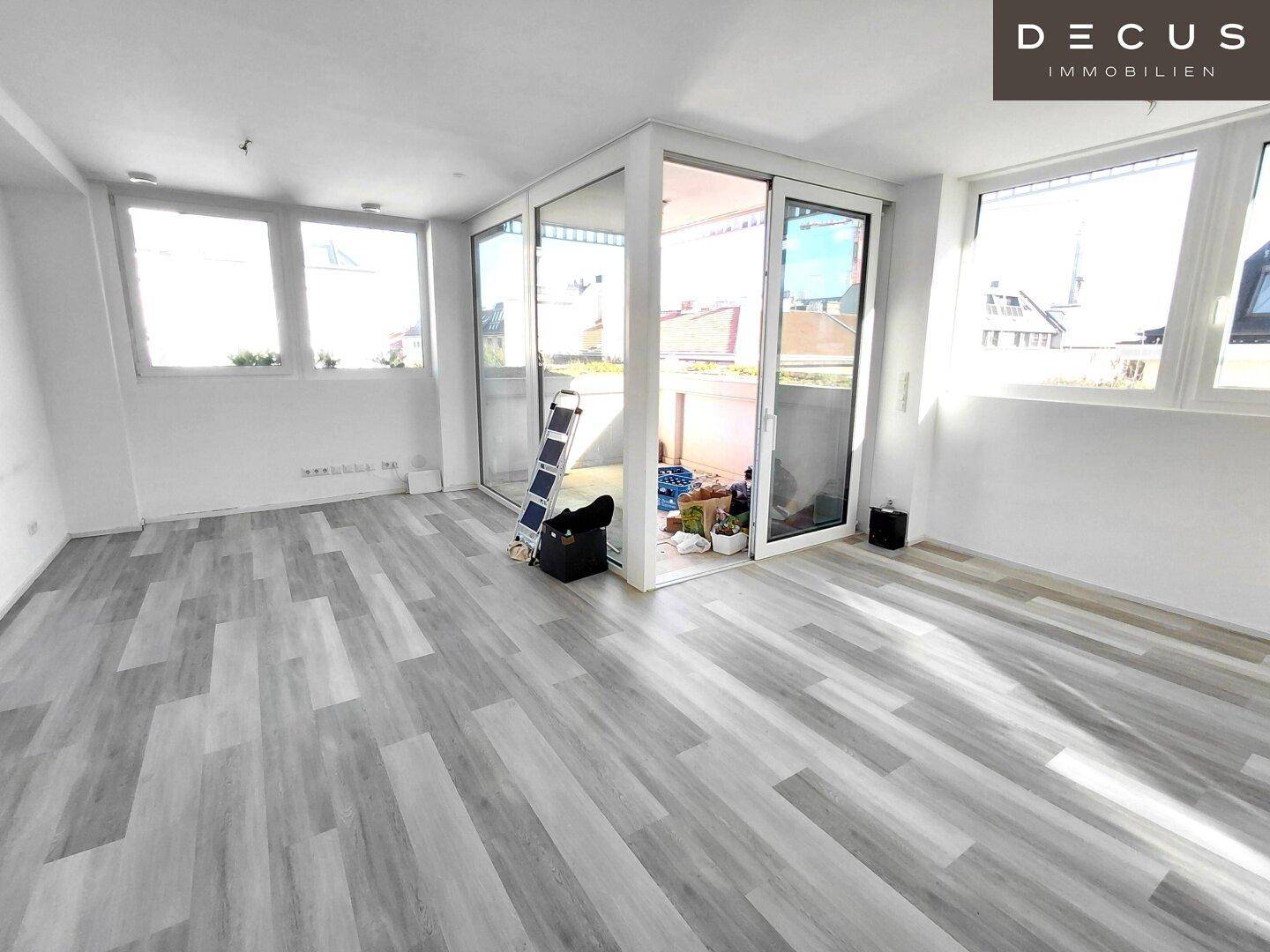 Geräumiger Wohnbereich mit großen Fenstern und Schiebetüren, die zu einer Terrasse führen.