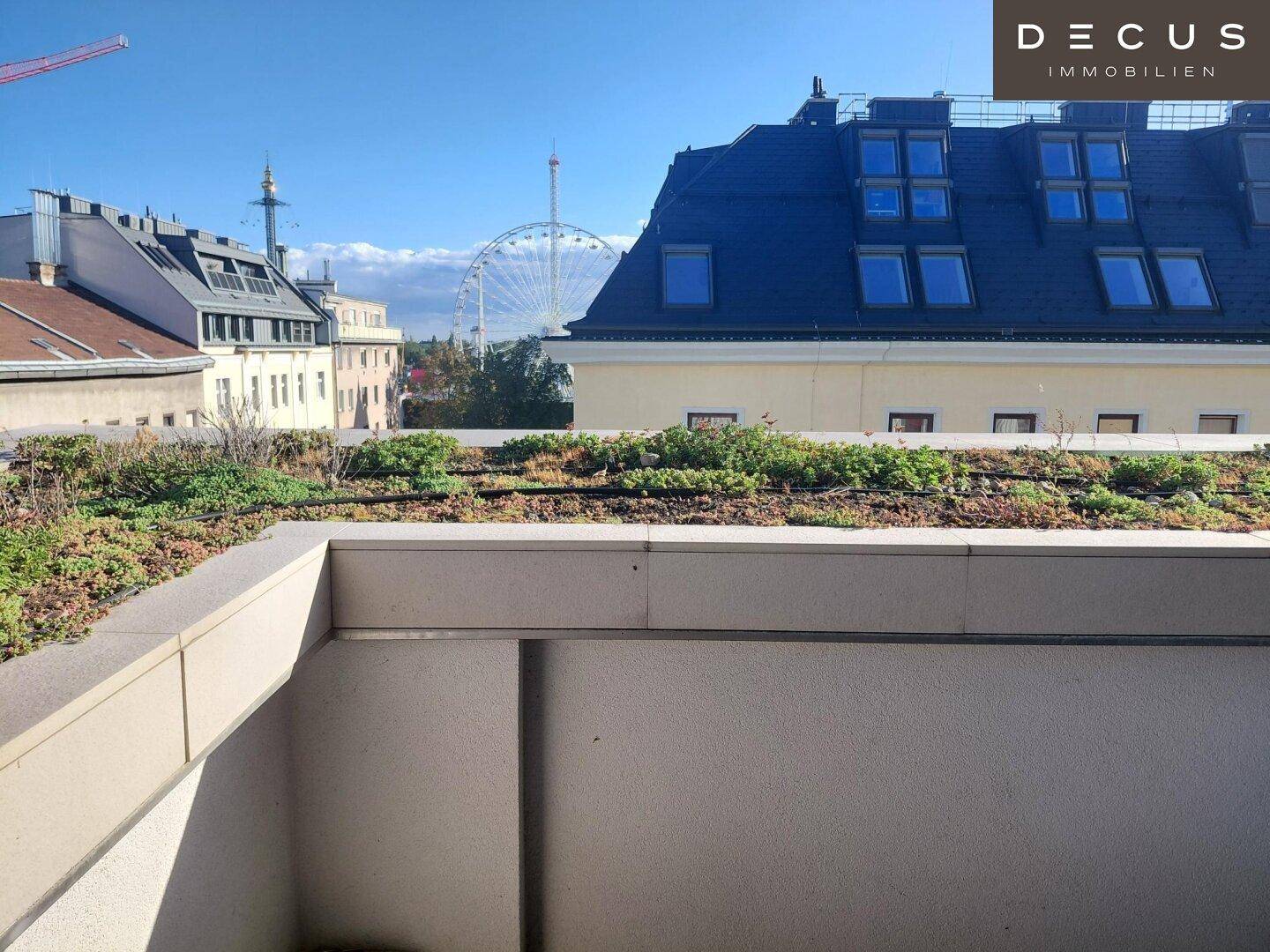 Dachterrasse mit Gründach und weitem Blick über die Stadt, inklusive Riesenrad im Hintergrund.