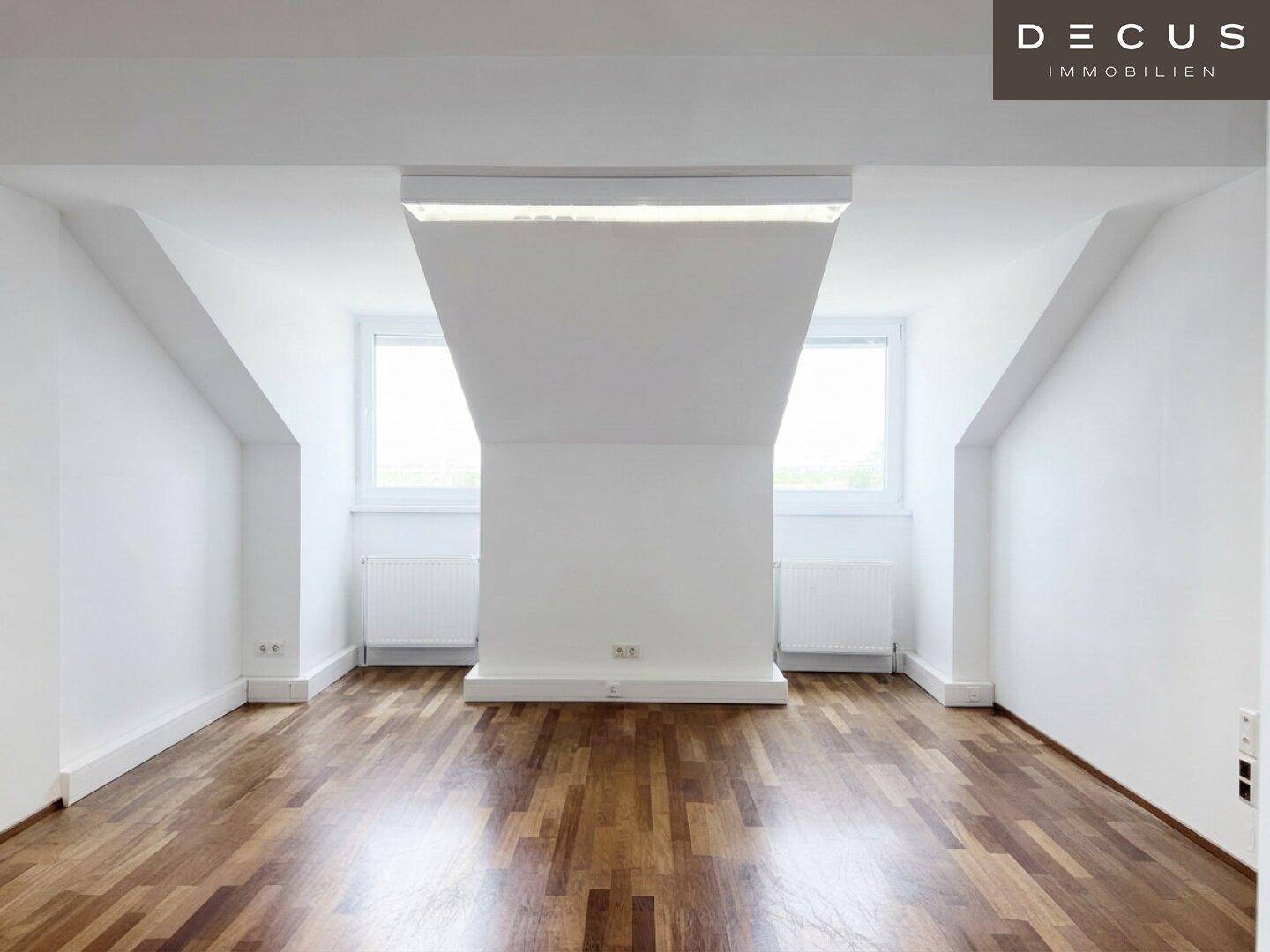 Leerer Büroraum mit Holzboden, zwei Fenstern und schrägen Decken, bereit für individuelle Gestaltung.