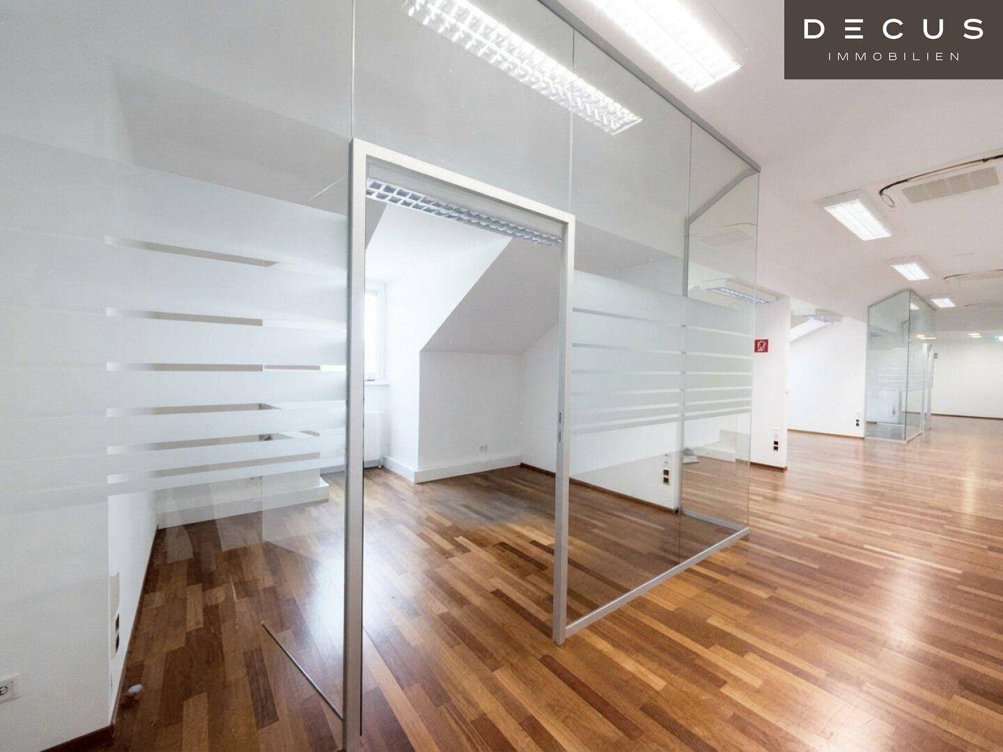 Geräumiges Büro mit Glaswänden, Holzboden und Blick auf eine Treppe, ideal für eine offene Arbeitsumgebung.