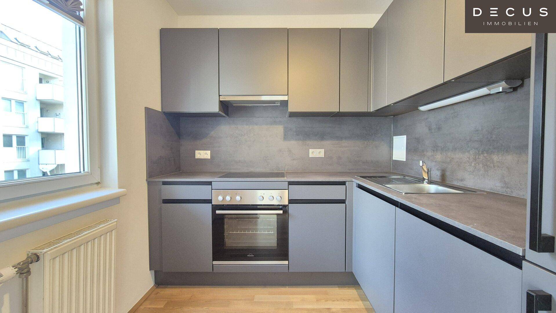 Moderne Einbauküche in Grau mit integriertem Backofen, Spüle und Fenster.