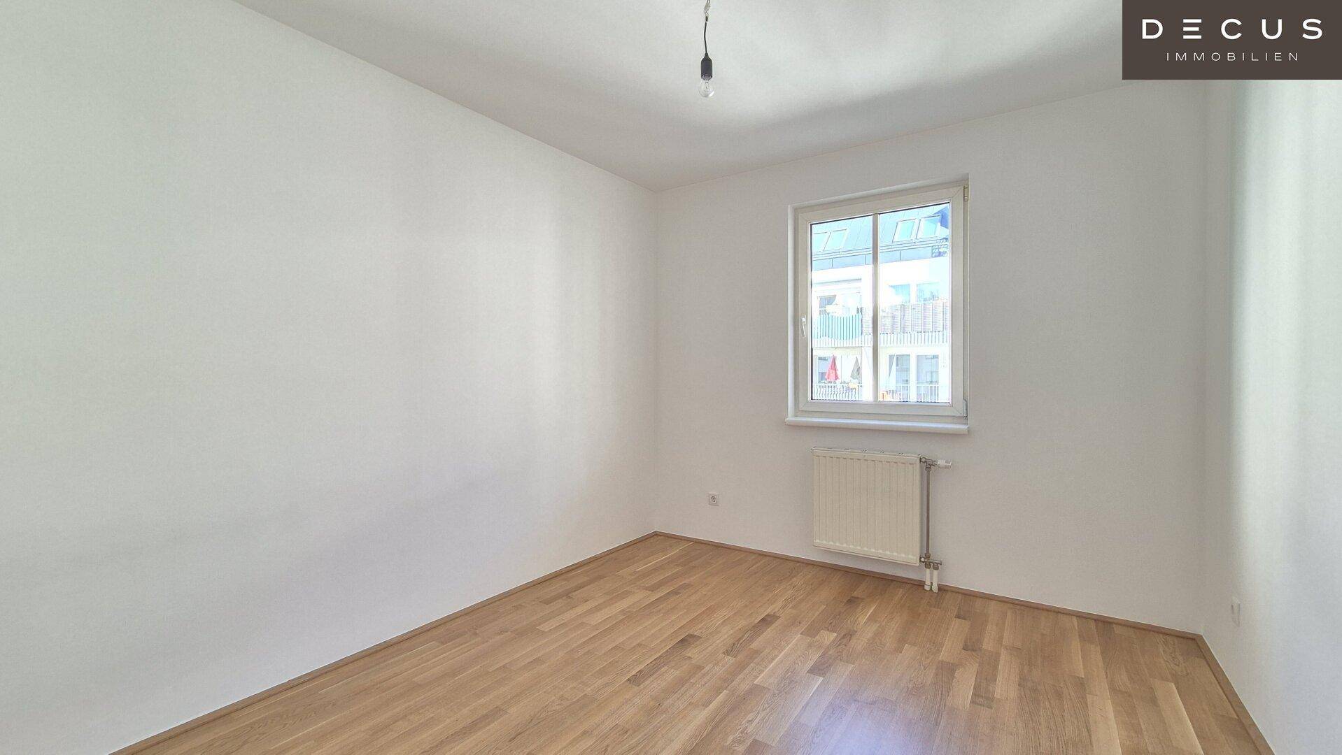 Helles Schlafzimmer mit Parkettboden und einem Fenster, das viel Tageslicht hereinlässt.