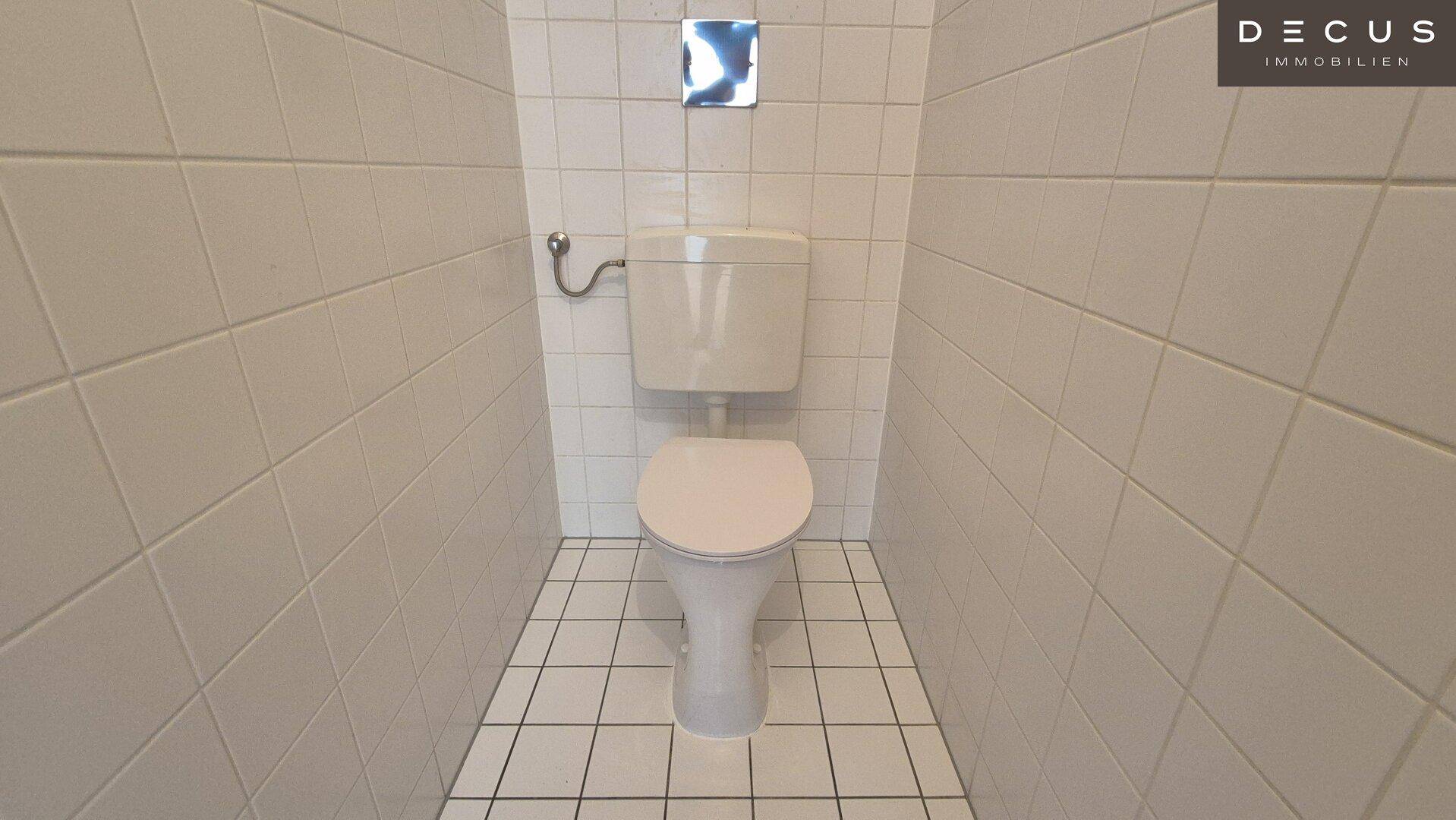 Separates WC mit weißen Fliesen an Wänden und Boden sowie einer Standard-Toilette.