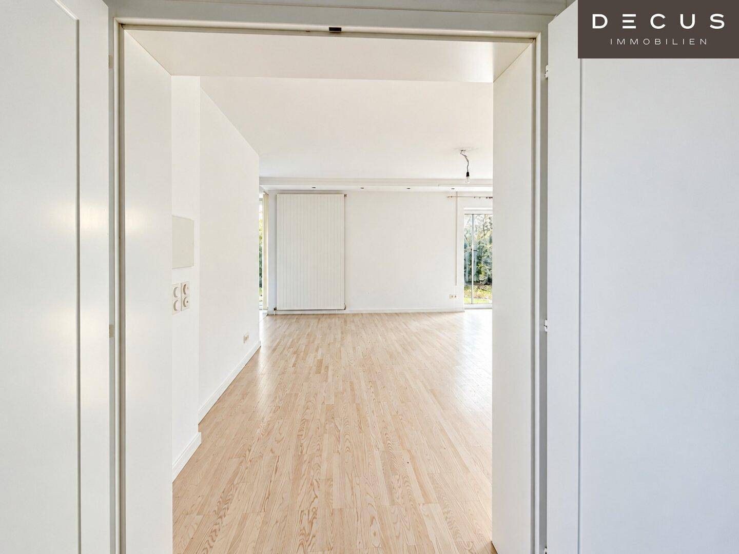 Blick durch eine Tür in einen hellen Raum mit Laminatboden und großen Fenstern.