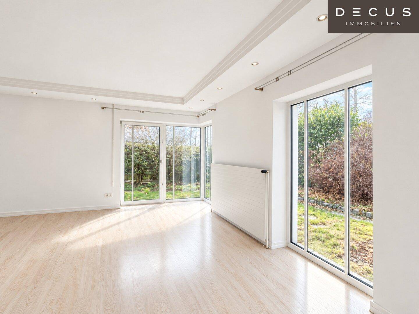Geräumiges Wohnzimmer mit hellem Laminatboden, großen Schiebetüren und Blick in den Garten.