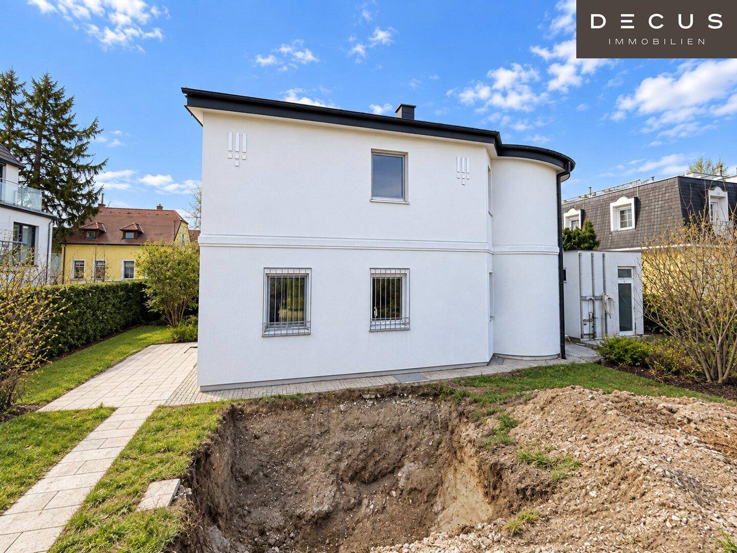 Seitenansicht des Hauses mit weißer Fassade und einer Baugrube im Vordergrund.