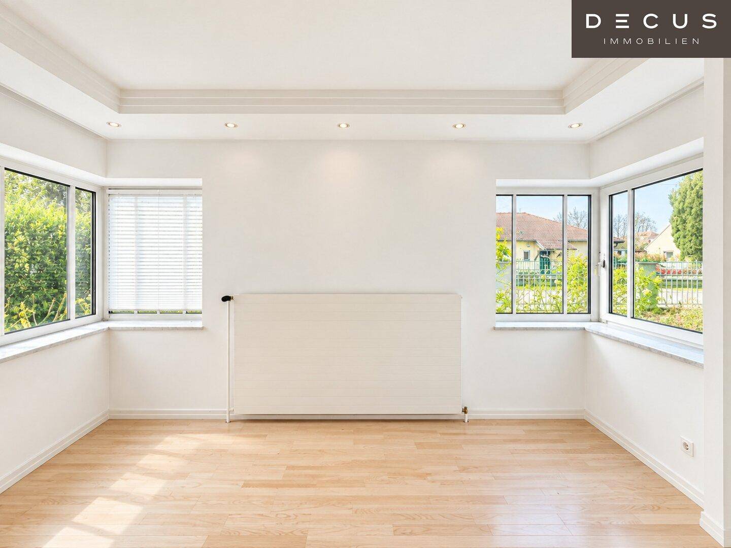 Heller Wohnraum mit Laminatboden, vielen Fenstern und indirekter Deckenbeleuchtung.