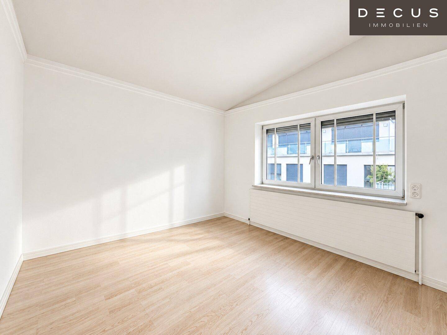 Helles Schlafzimmer mit Laminatboden, Dachschräge und Fenster mit Blick nach draußen.