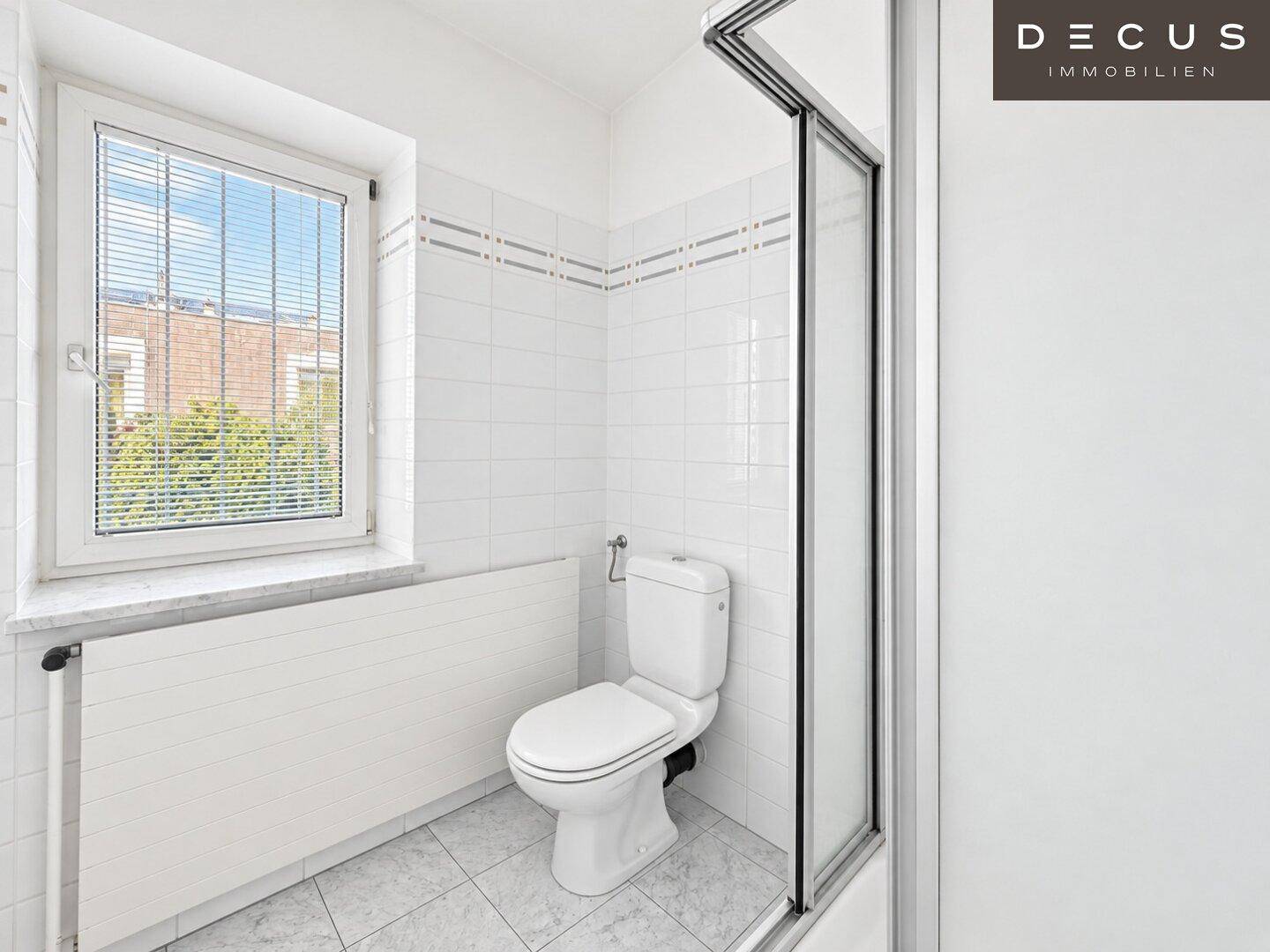 Kleines Badezimmer mit weißen Fliesen, Toilette, Duschkabine und Fenster.