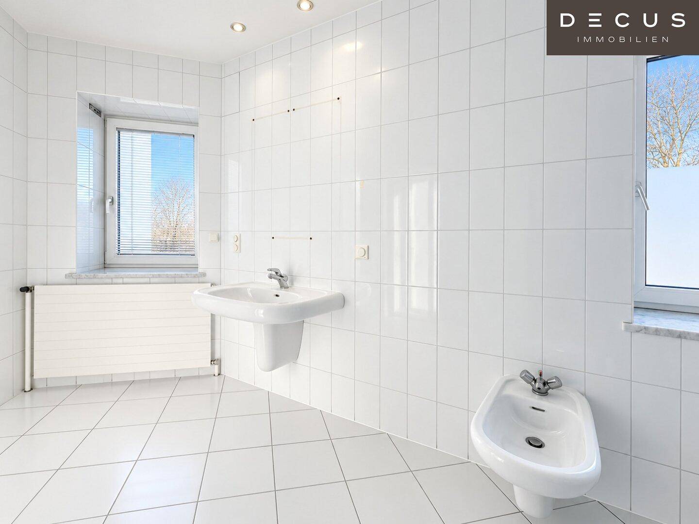 Helles Badezimmer mit weißen Fliesen, Waschbecken, Bidet und Fenster.