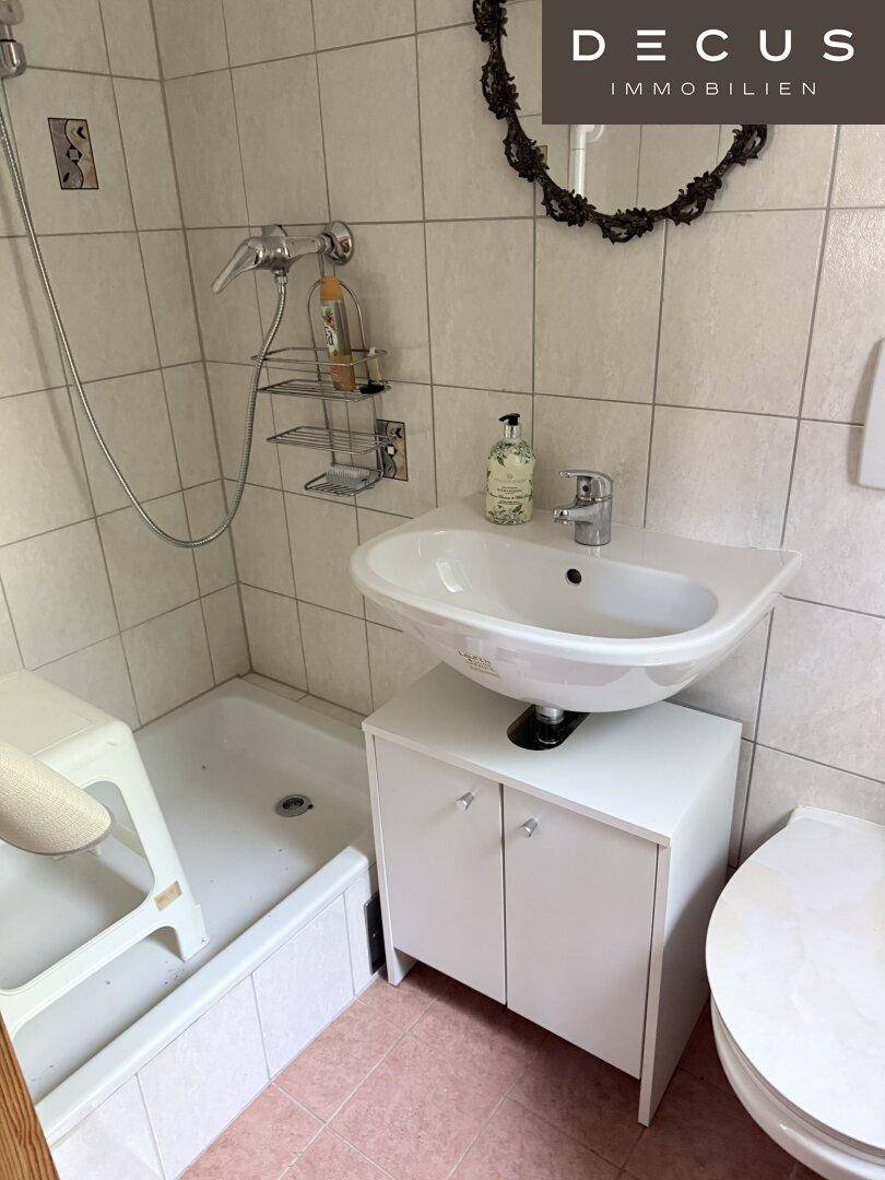 Badezimmer mit Dusche, Waschbecken und WC, funktional und hell gefliest.