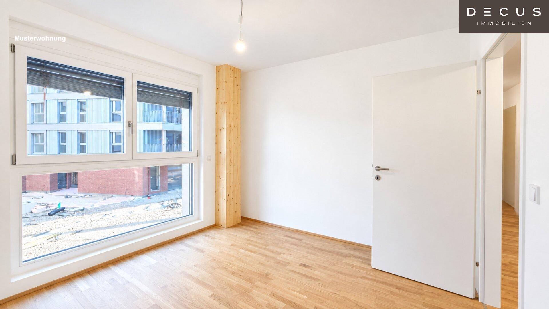 Geräumiges Zimmer mit hellem Holzfußboden und großen Fenstern, die viel Tageslicht hereinlassen.
