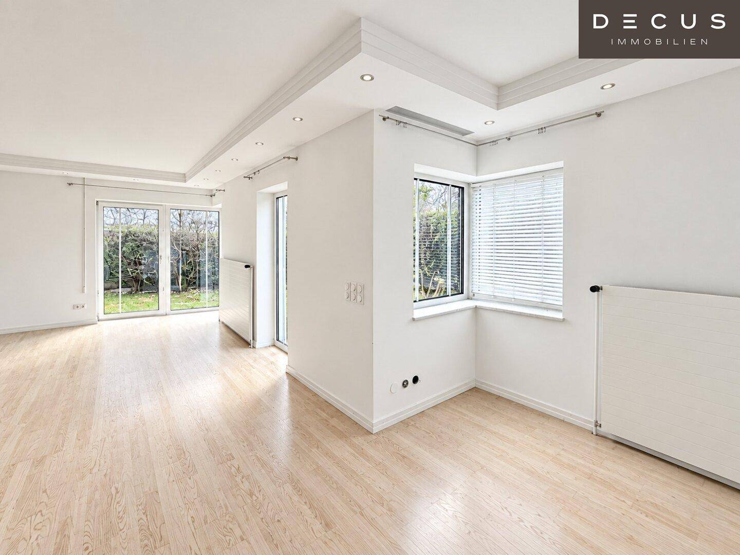 Helles Wohnzimmer mit Laminatboden, großen Fenstern und indirekter Deckenbeleuchtung.