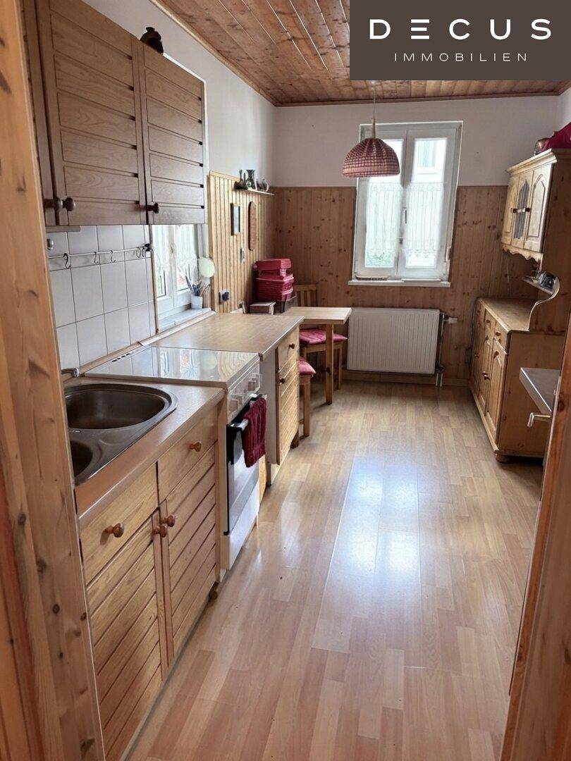 Gemütliche Küche mit Holzschränken, Essbereich und Blick auf den Garten durch das Fenster.
