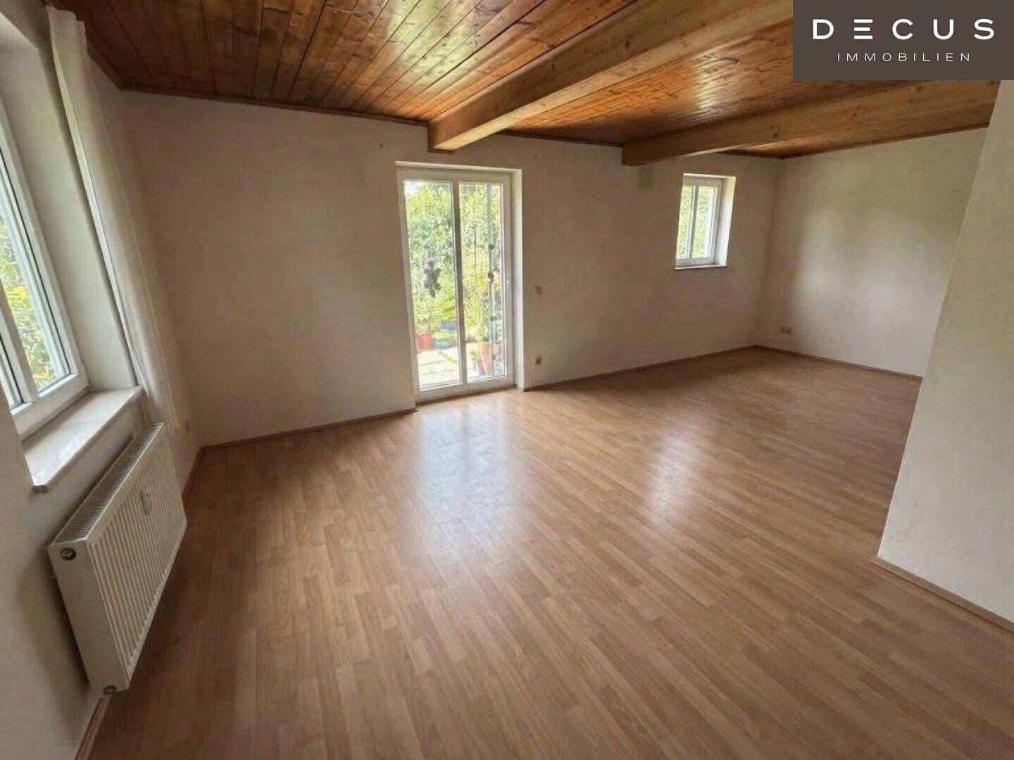 Helles Wohnzimmer mit Zugang zum Balkon und Holzbalkendecke, bietet viel natürliches Licht.