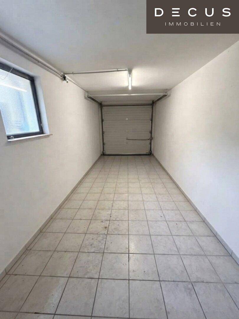 Geräumige Garage mit Fliesenboden und Rolltor, bietet Platz für ein Fahrzeug und Lagerung.