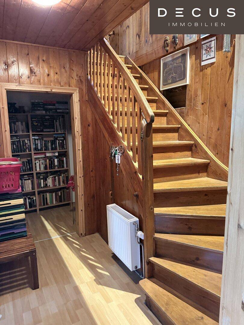 Rustikaler Treppenaufgang aus Holz mit Holzvertäfelung und Blick in einen Raum mit Bücherregalen.