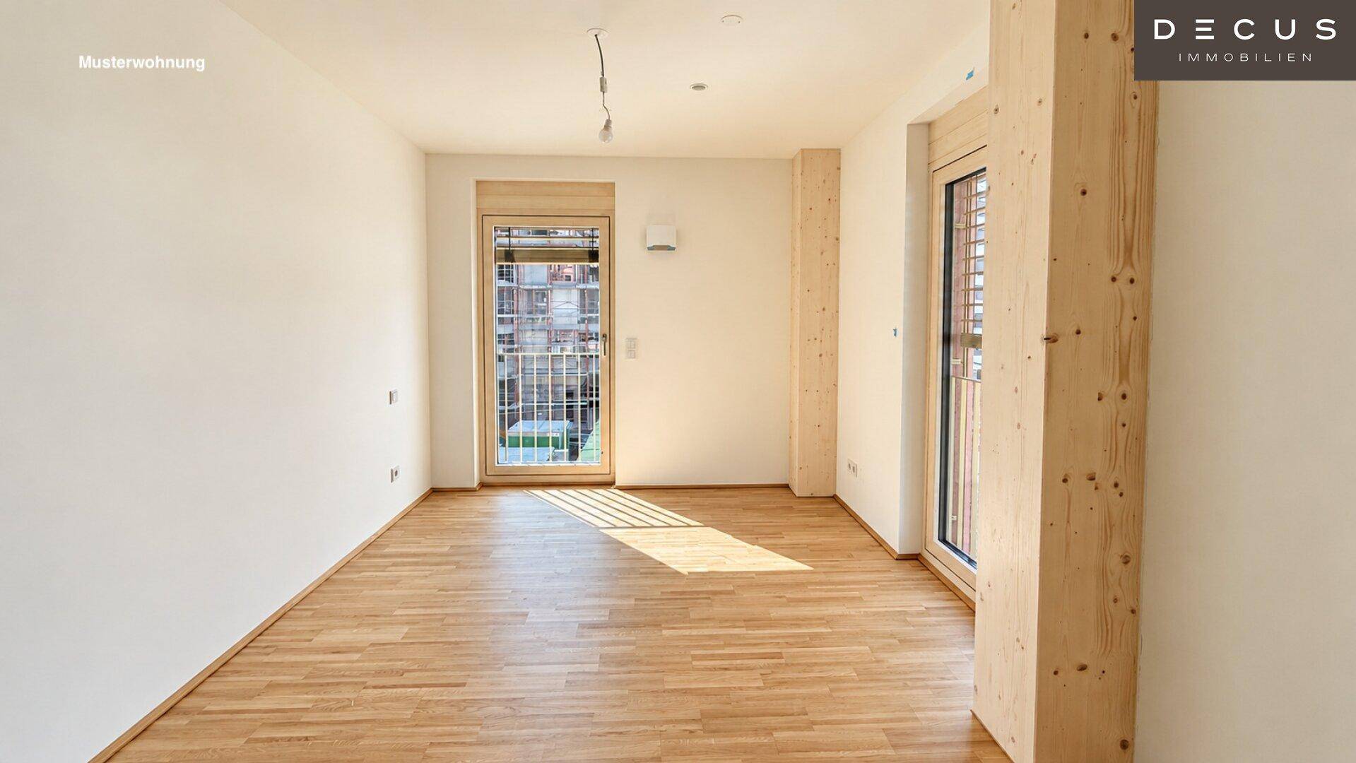 Leerer Raum einer Musterwohnung mit Holzboden, weißen Wänden und Balkonzugang.