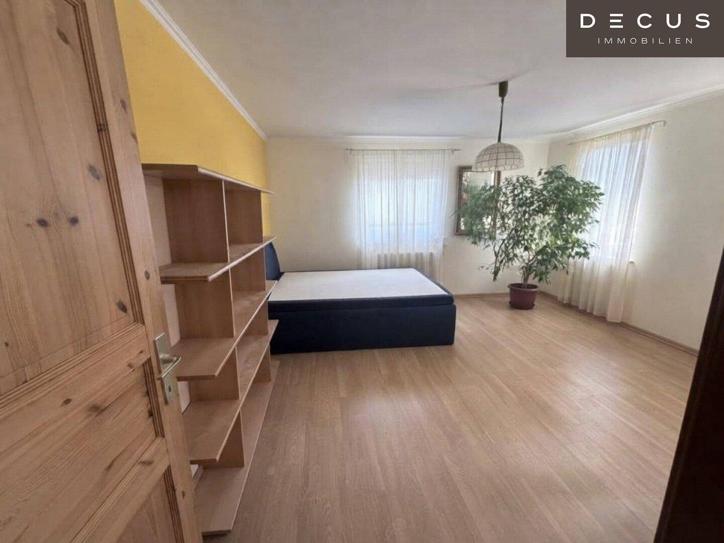 Helles Schlafzimmer mit Laminatboden, gelber Akzentwand und großem Fenster.