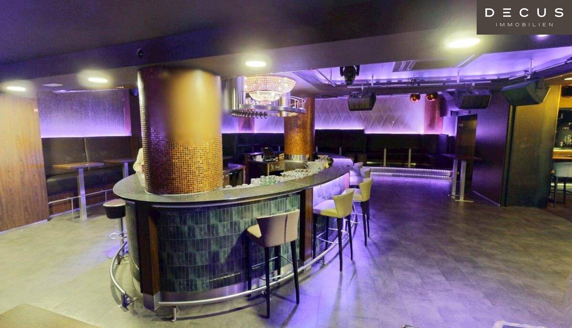 Großer Nachtclub mit beleuchteter Bar, Tanzfläche und Sitznischen, alles in lebhaftem Lila beleuchtet.