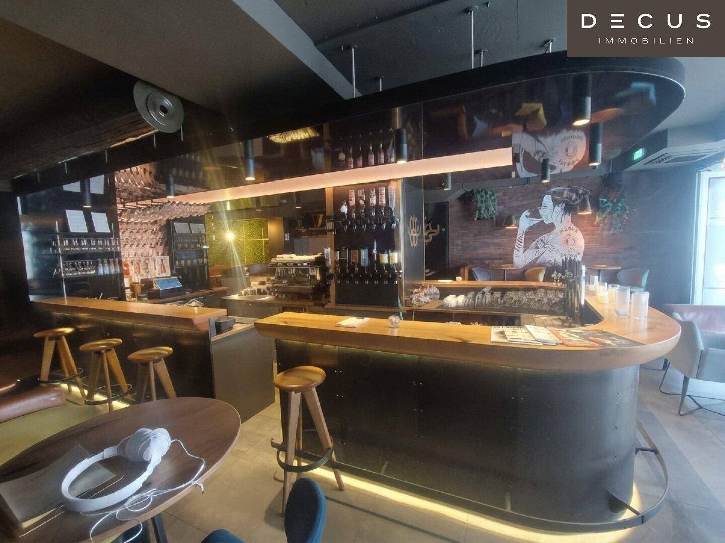 Geräumige Bar mit dunkler Theke, Holzstühlen und einer reflektierenden Decke, die den Raum modern wirken lässt.