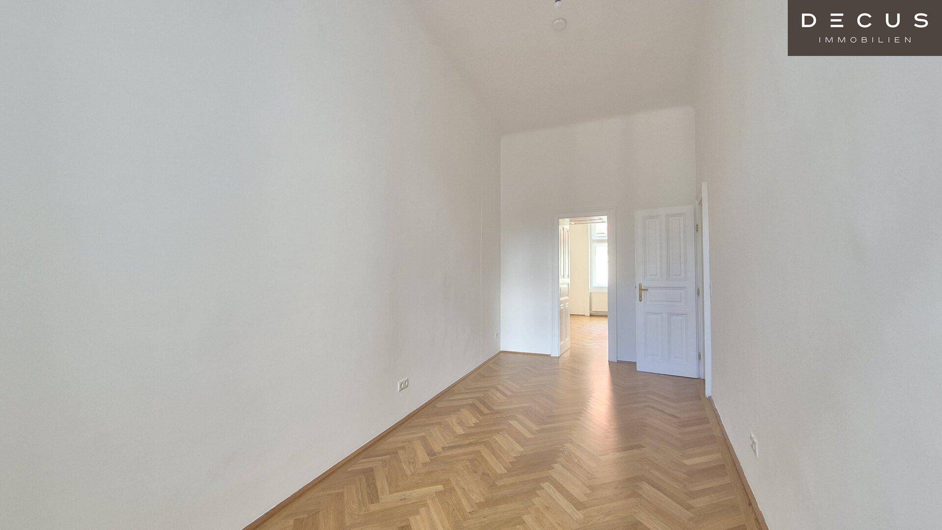 Leeres Zimmer mit klassischem Fischgrätparkett und Zugang zu weiteren Räumen.