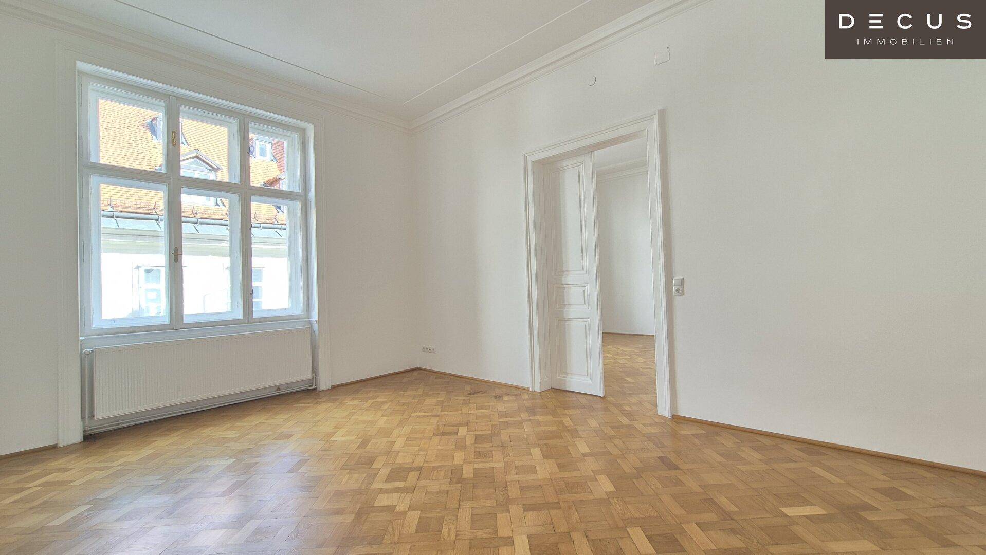 Geräumiges Zimmer mit Fischgrätparkett, hohen Decken und großen Fenstern.