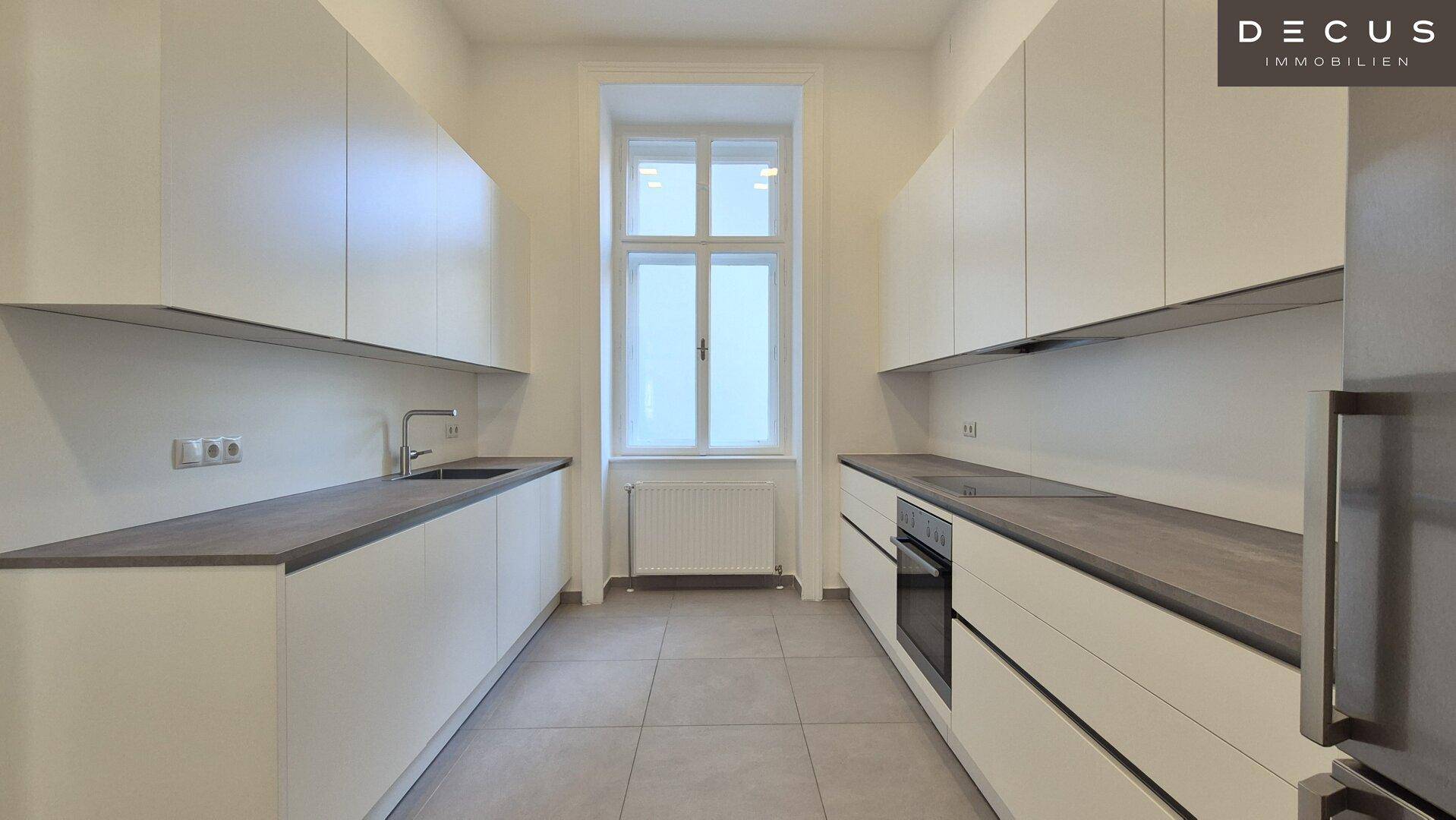 Moderne Küche mit weißen Schränken, dunklen Arbeitsplatten und Fenster für Tageslicht.