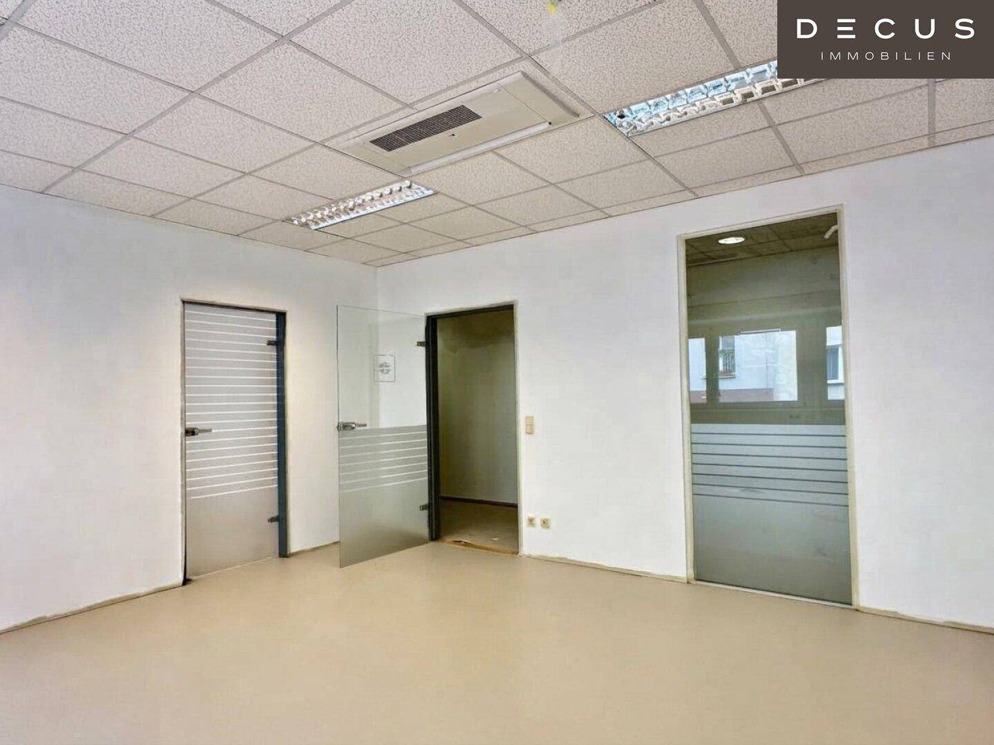 Leerer Büroraum mit Rasterdecke, Leuchtstofflampen und modernen Glastüren.