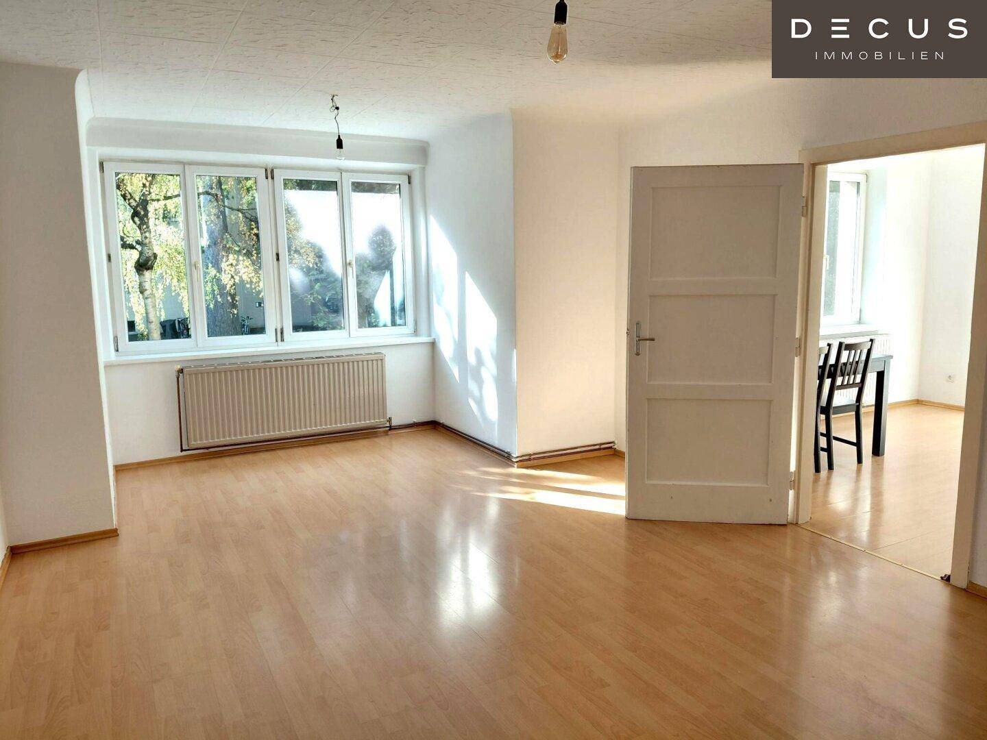 Geräumiges, helles Wohnzimmer mit Laminatboden und Zugang zu einem weiteren Raum.