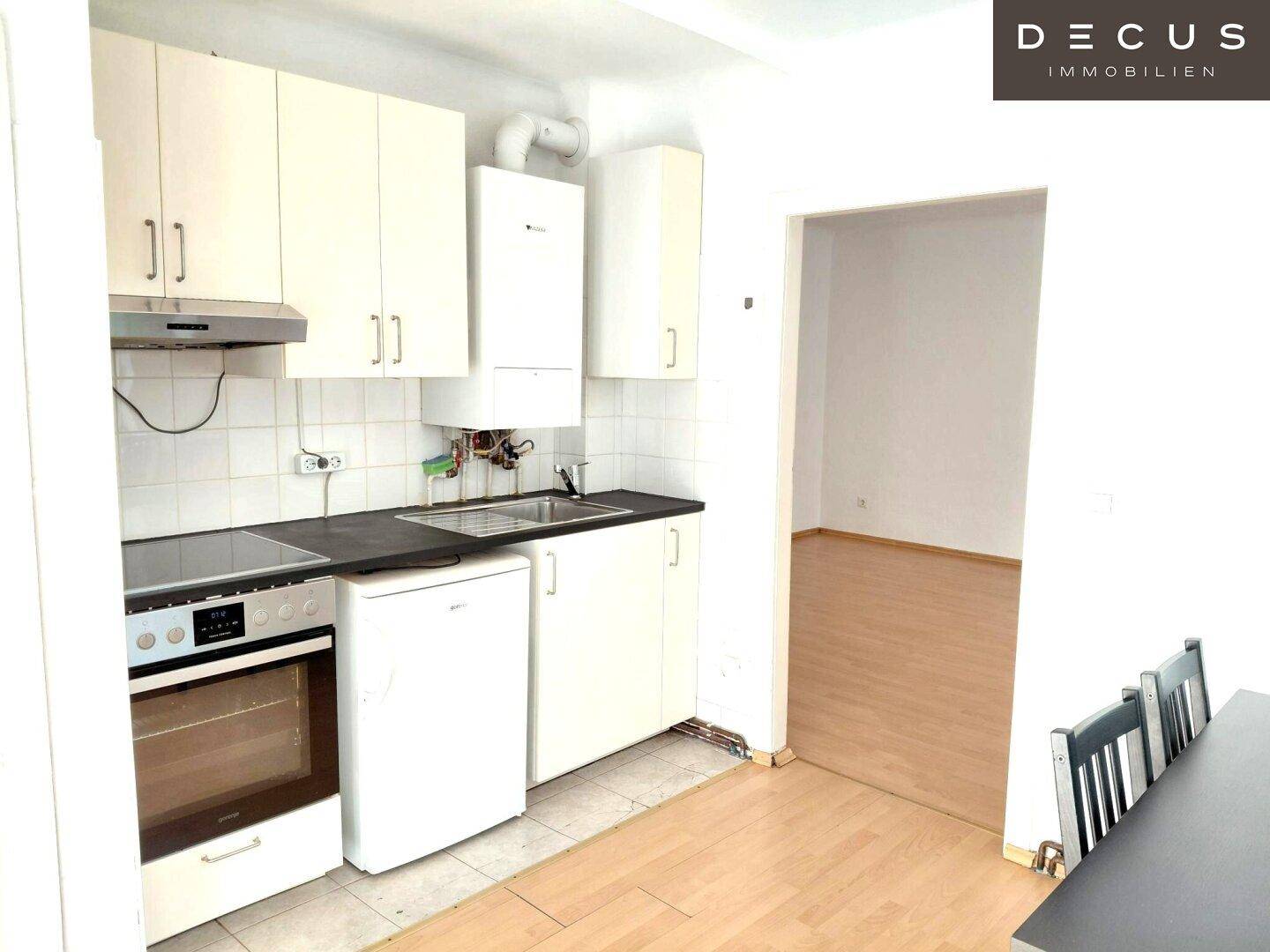 Funktionale Küche mit weißen Schränken, Herd, Kühlschrank und Gastherme.