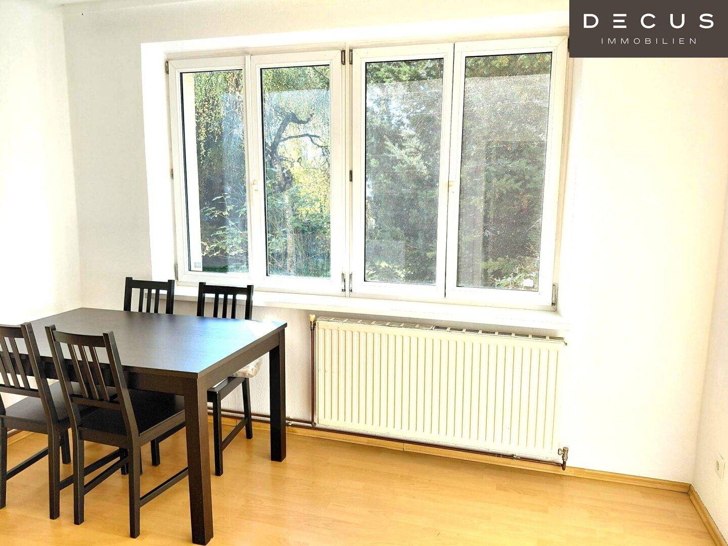 Heller Essbereich mit dunklem Holztisch und Stühlen neben einem großen Fenster.