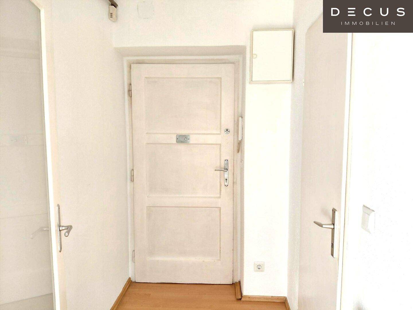 Heller Eingangsbereich mit weißer Tür, Gegensprechanlage und Laminatboden.