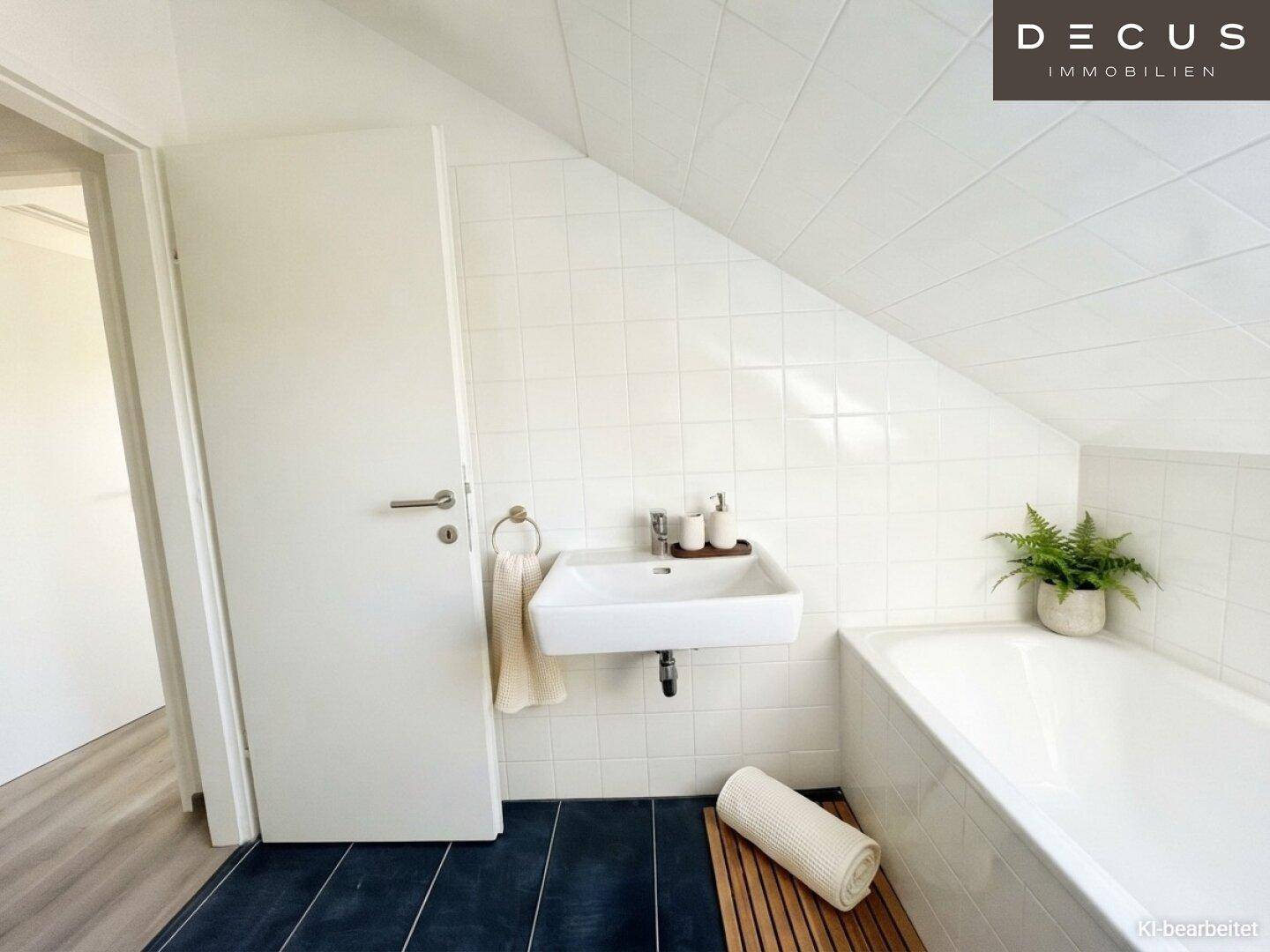 Modernes Badezimmer im Dachgeschoss mit weiß gefliesten Wänden, dunklem Boden und einer Badewanne unter der Schräge.