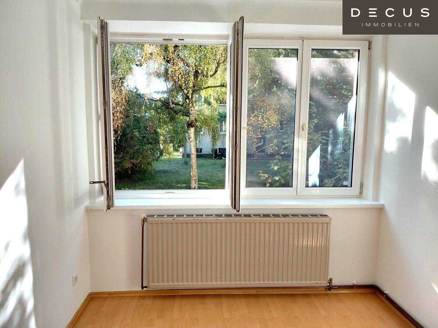 Heller Raum mit großem Fenster, das einen Blick ins Grüne bietet, und einem Heizkörper.