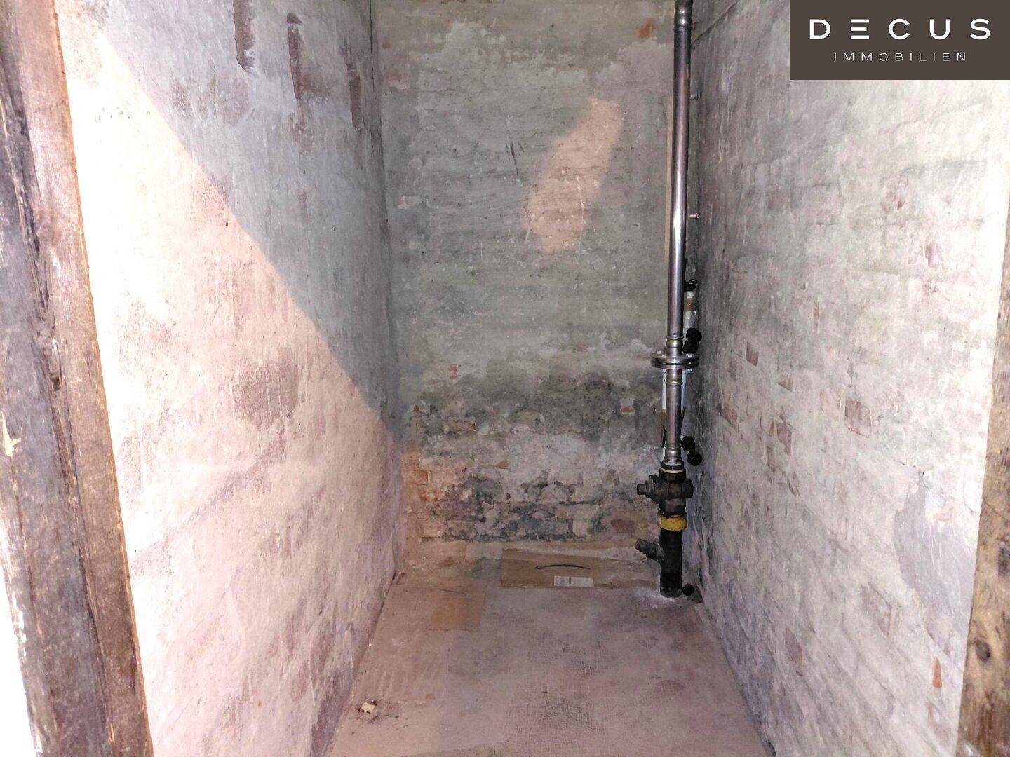 Einfacher Abstellraum oder Kellerabteil mit unverputzten Ziegelwänden und sichtbaren Rohren.