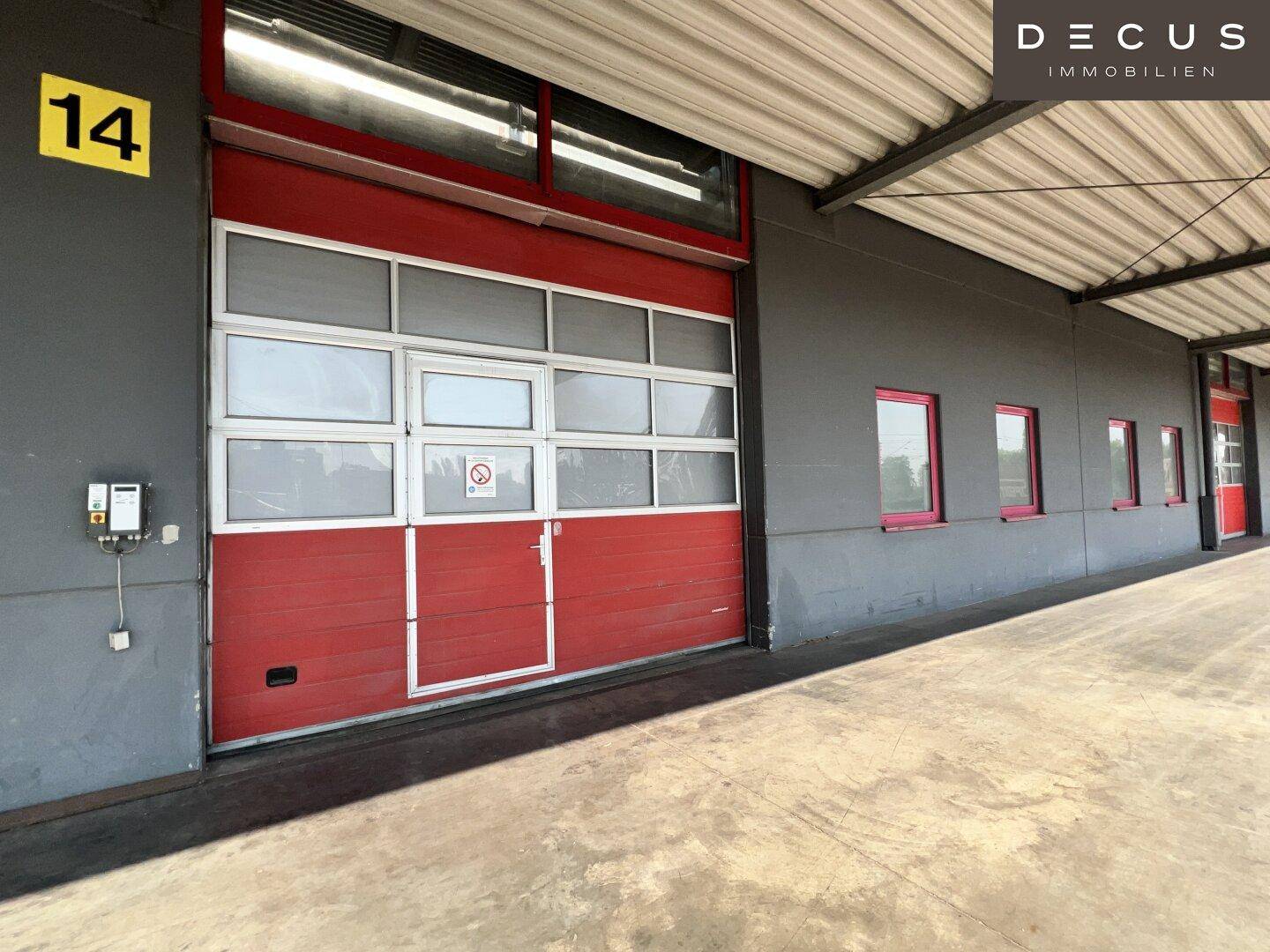 Rotes Sektionaltor mit integrierter Tür und Fenstern an der Fassade eines Lagergebäudes.