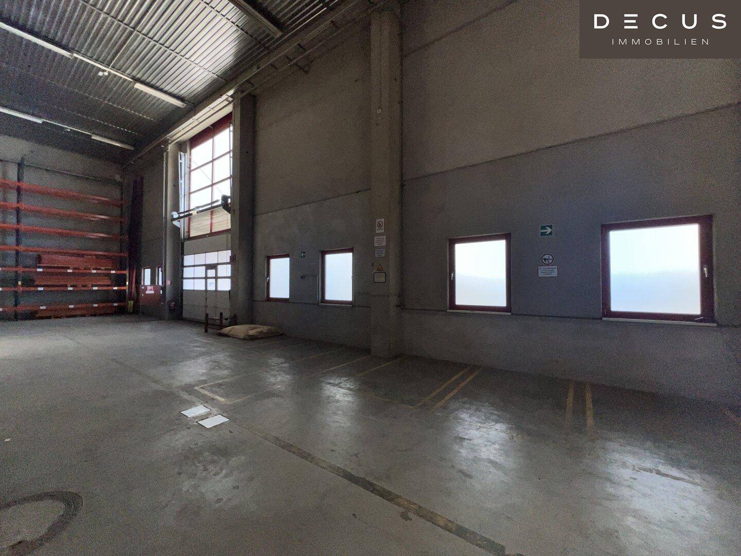 Leere Lagerhalle mit hohen Decken, Betonboden und großen Fenstern, bereit zur Nutzung.