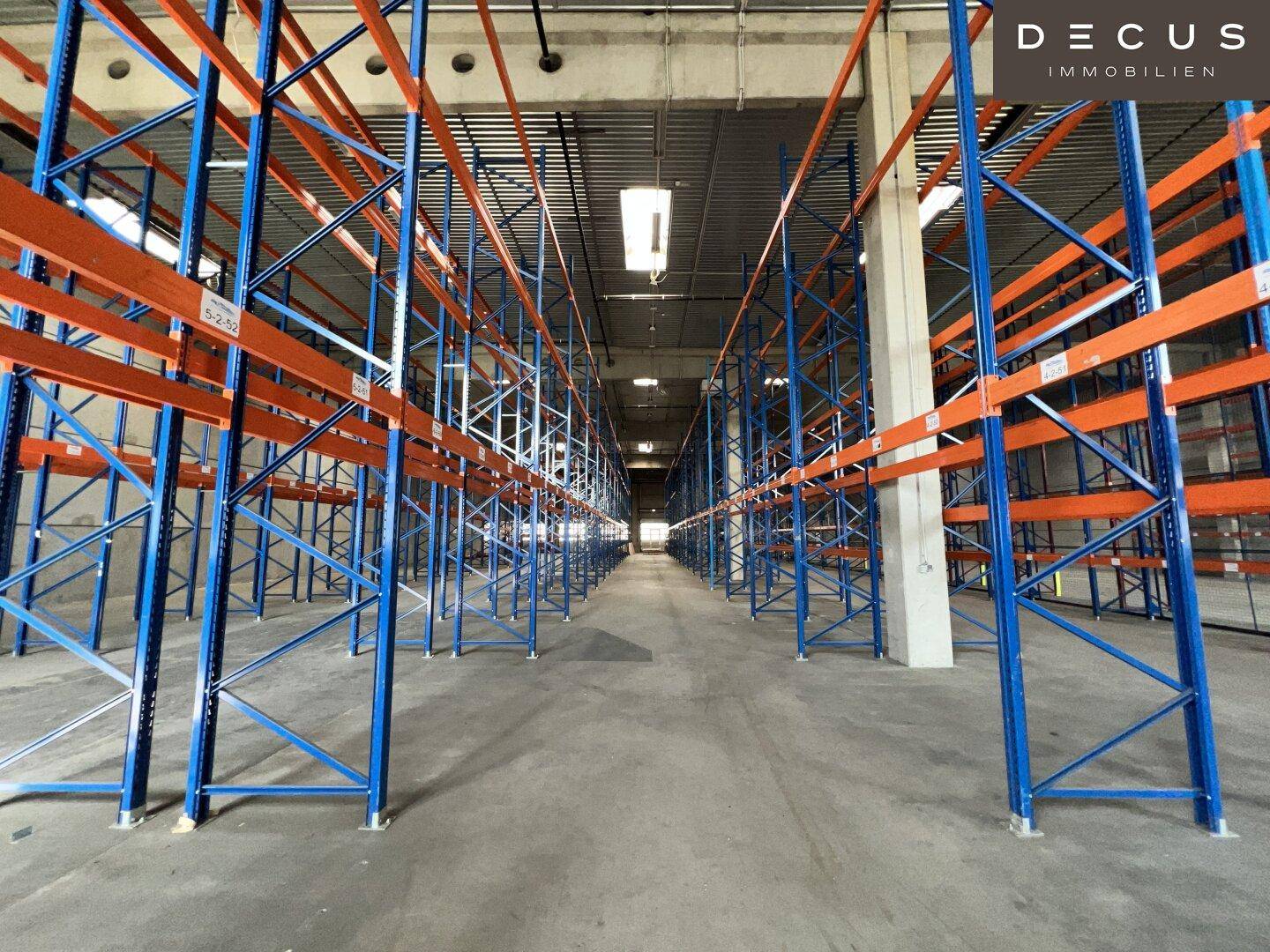 Weitläufige Lagerhalle mit Reihen von blauen und orangen Hochregalen und Betonboden.