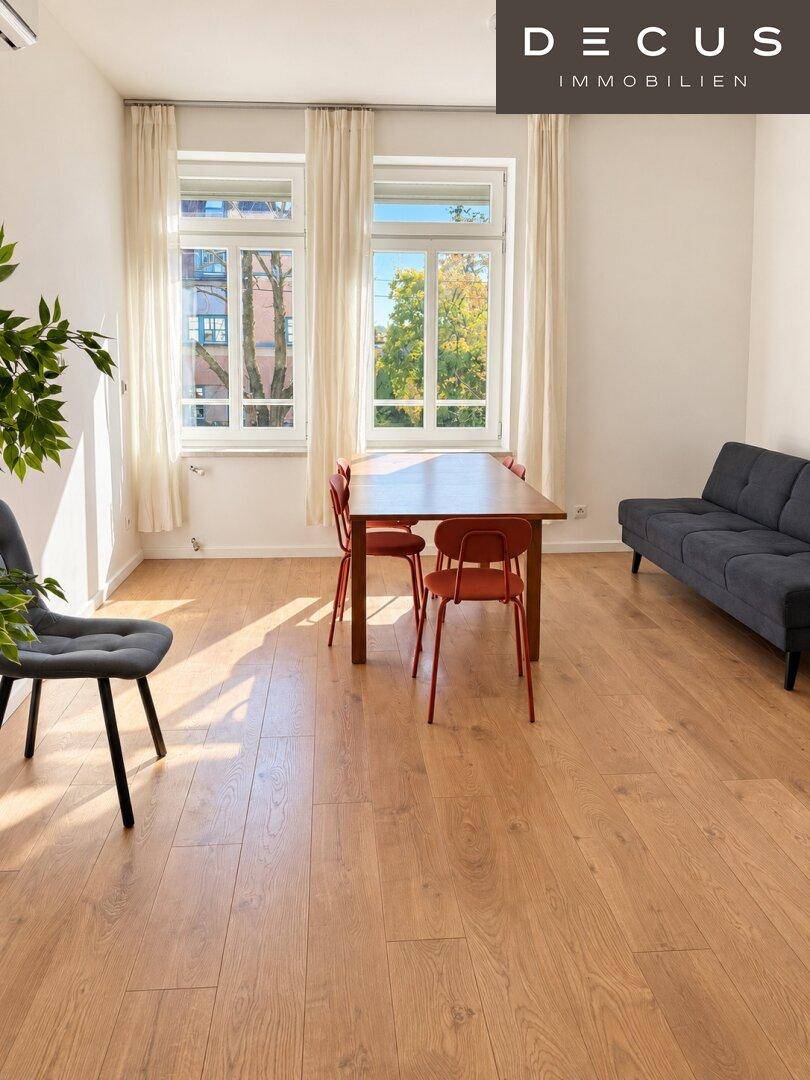 Heller Wohn- und Essbereich mit Holzboden, großen Fenstern und moderner Einrichtung.