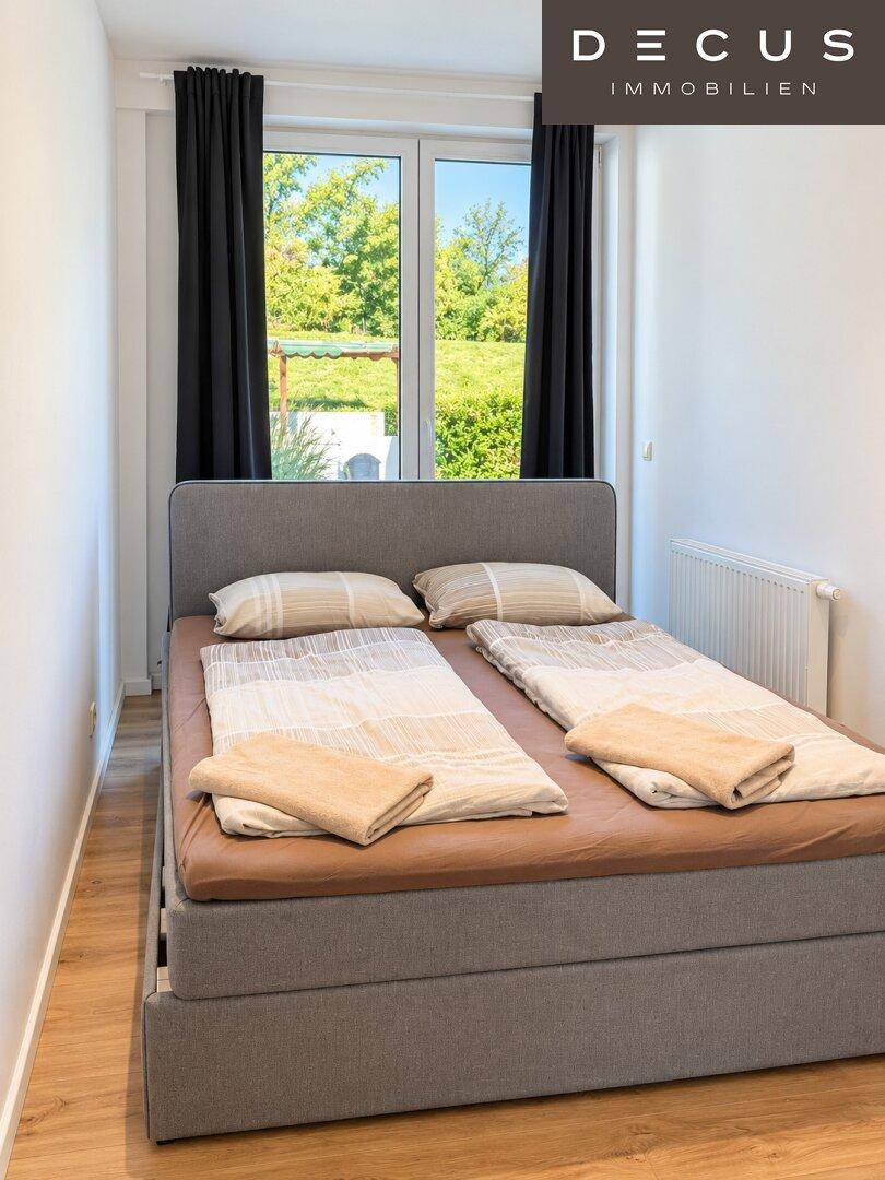 Helles Schlafzimmer mit Doppelbett, Holzboden und Blick ins Grüne.