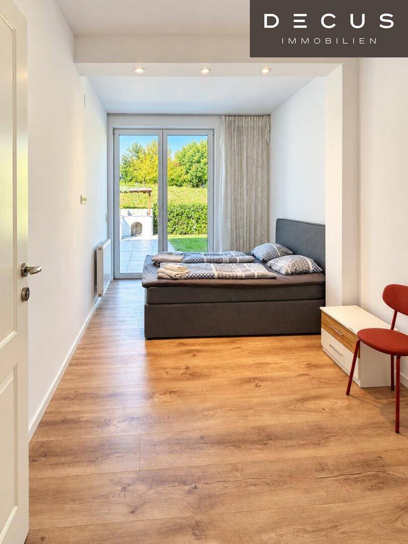 Schlafzimmer mit Doppelbett, Holzboden und direktem Zugang zur Terrasse mit Gartenblick.