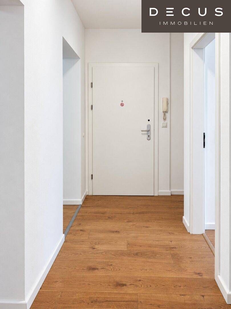 Heller Flur mit Holzboden und weißer Eingangstür, der zu den weiteren Räumen führt.