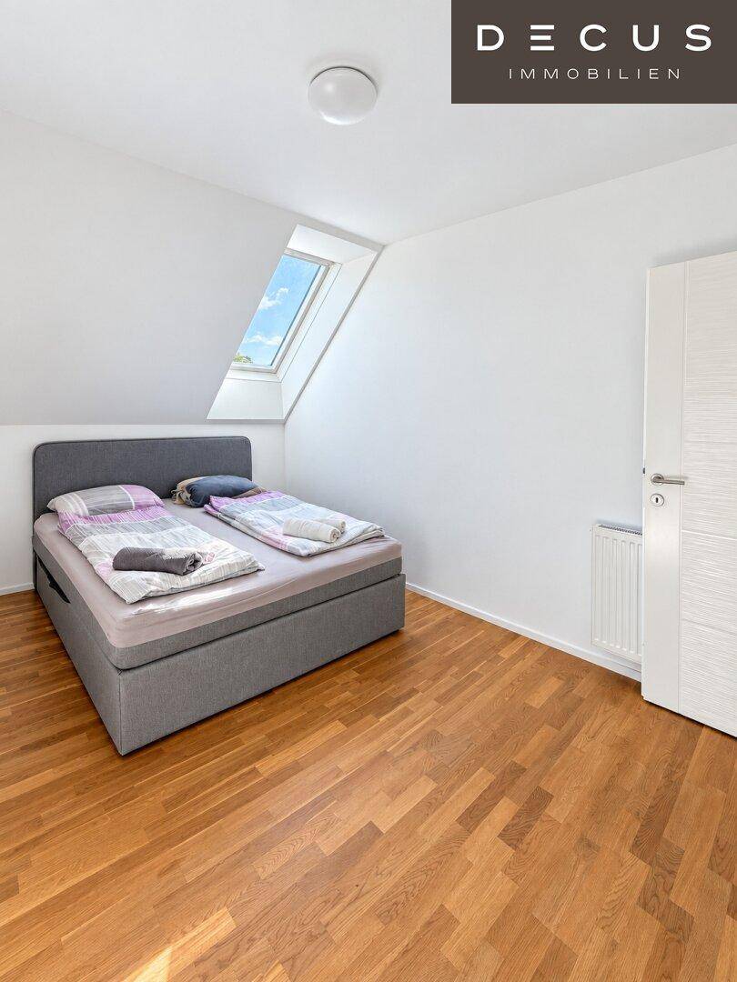 Helles Schlafzimmer im Dachgeschoss mit Holzboden und einem schrägen Dachfenster.