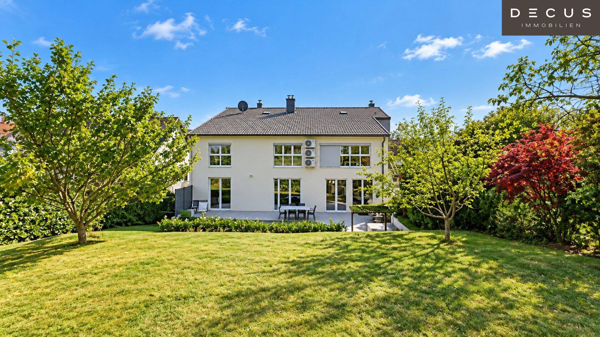 Großer, gepflegter Garten mit Rasenfläche, Bäumen und einer kleinen Terrasse am Haus.